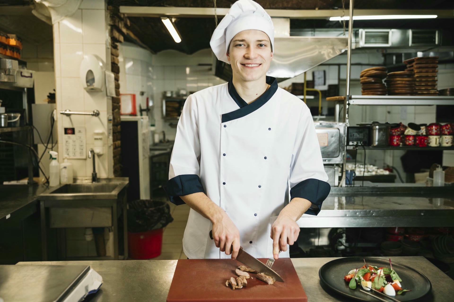cook cutting roasted meat board near salad plate scaled